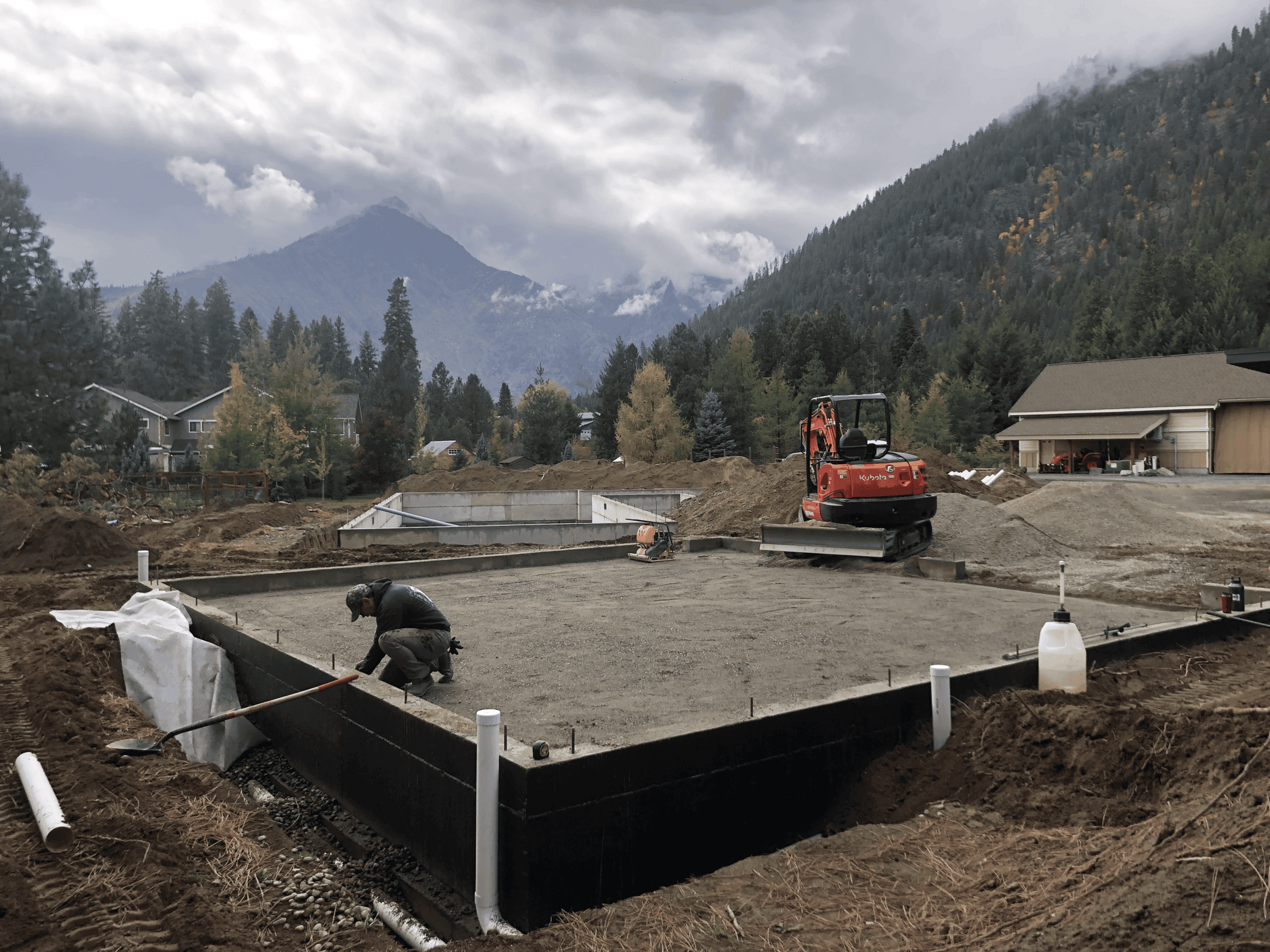 Foundation of a residential home with excavator and mountains in the background